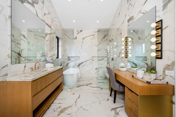 A modern luxury bathroom featuring white marble wall tiles, a wooden vanity, and large mirrors.