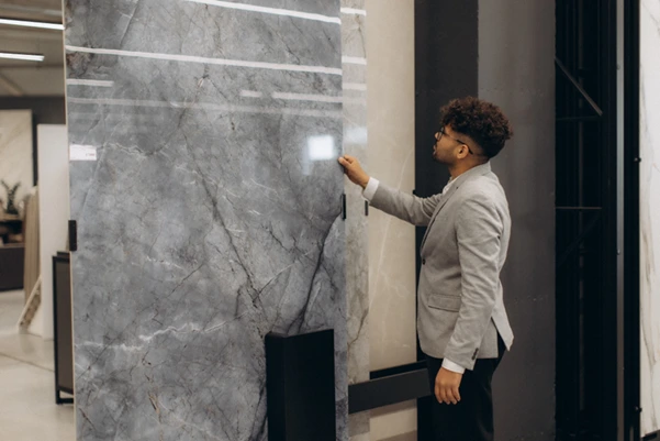 A customer inspecting a large, grey and white luxury marble tile slab in a showroom.