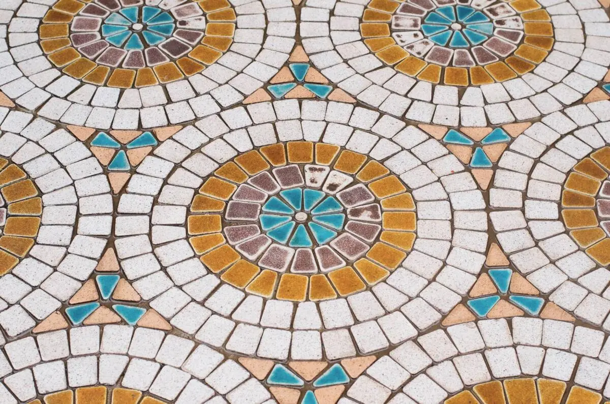 A close-up of a circular and geometric mosaic floor design featuring blue, yellow, and white ceramic tiles.