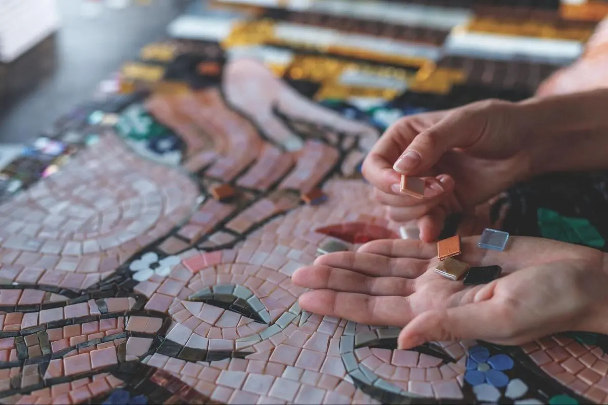 Female hands holding a variety of small, colorful mosaic tiles to choose a design for a kitchen splashback renovation.