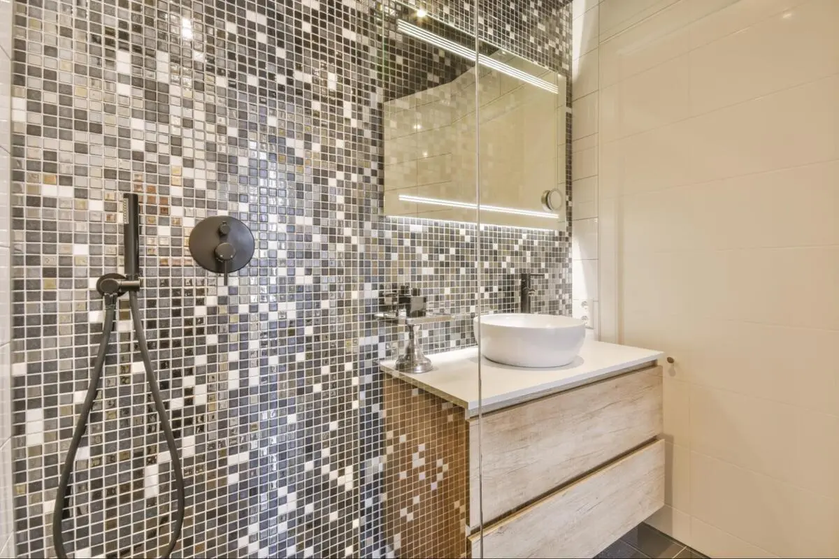 Bathroom feature wall covered in metallic glass mosaic tiles with a vessel sink and a shower fixture