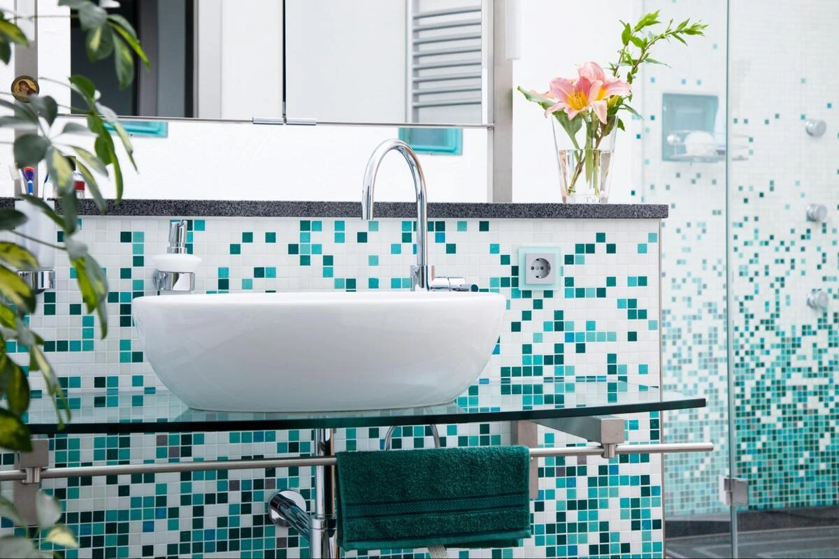 Bathroom vanity with teal mosaic tile walls and white basin showing mosaic tile installation in a wet area