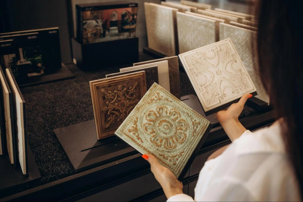 Woman holding a decorative ceramic tile while browsing samples in a tile showroom